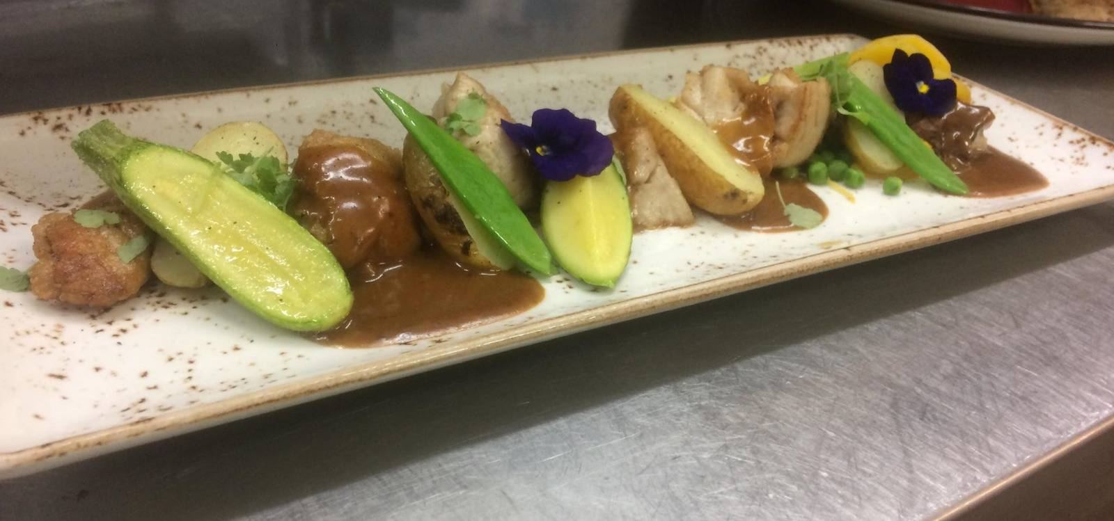 Assiette longue de légumes rôtis, courgette, haricots et fleurs comestibles, nappée de jus