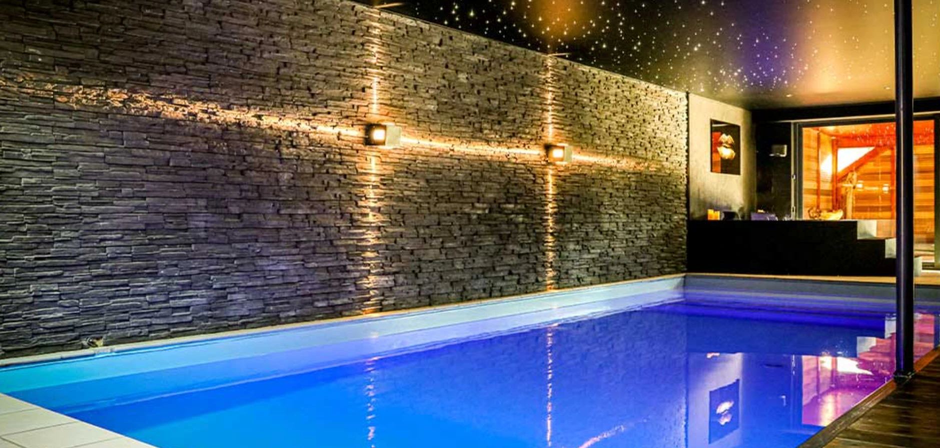 Piscine intérieure éclairée d'une suite, mur de pierre