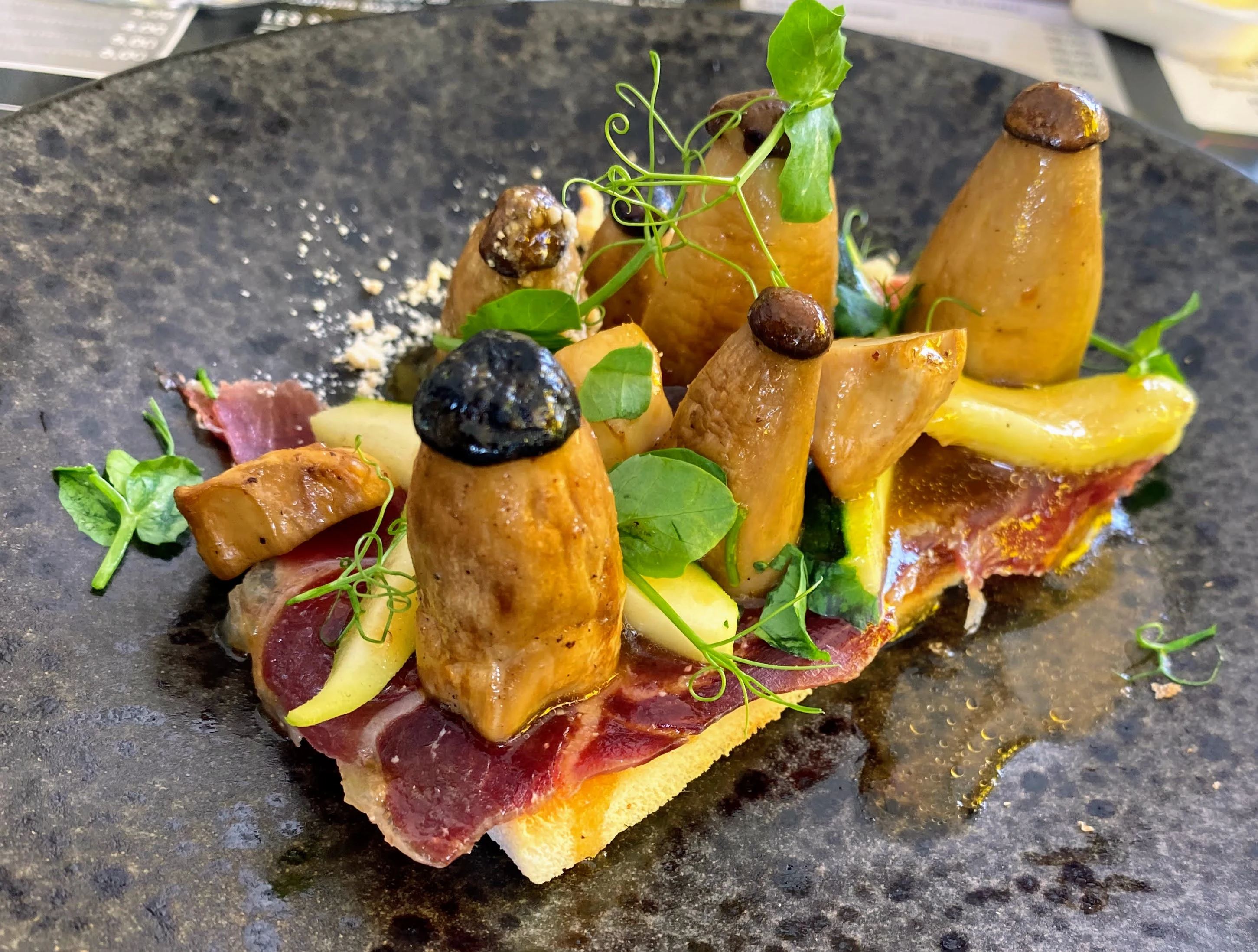 Cèpes, jambon cru et pousses sur une assiette noire