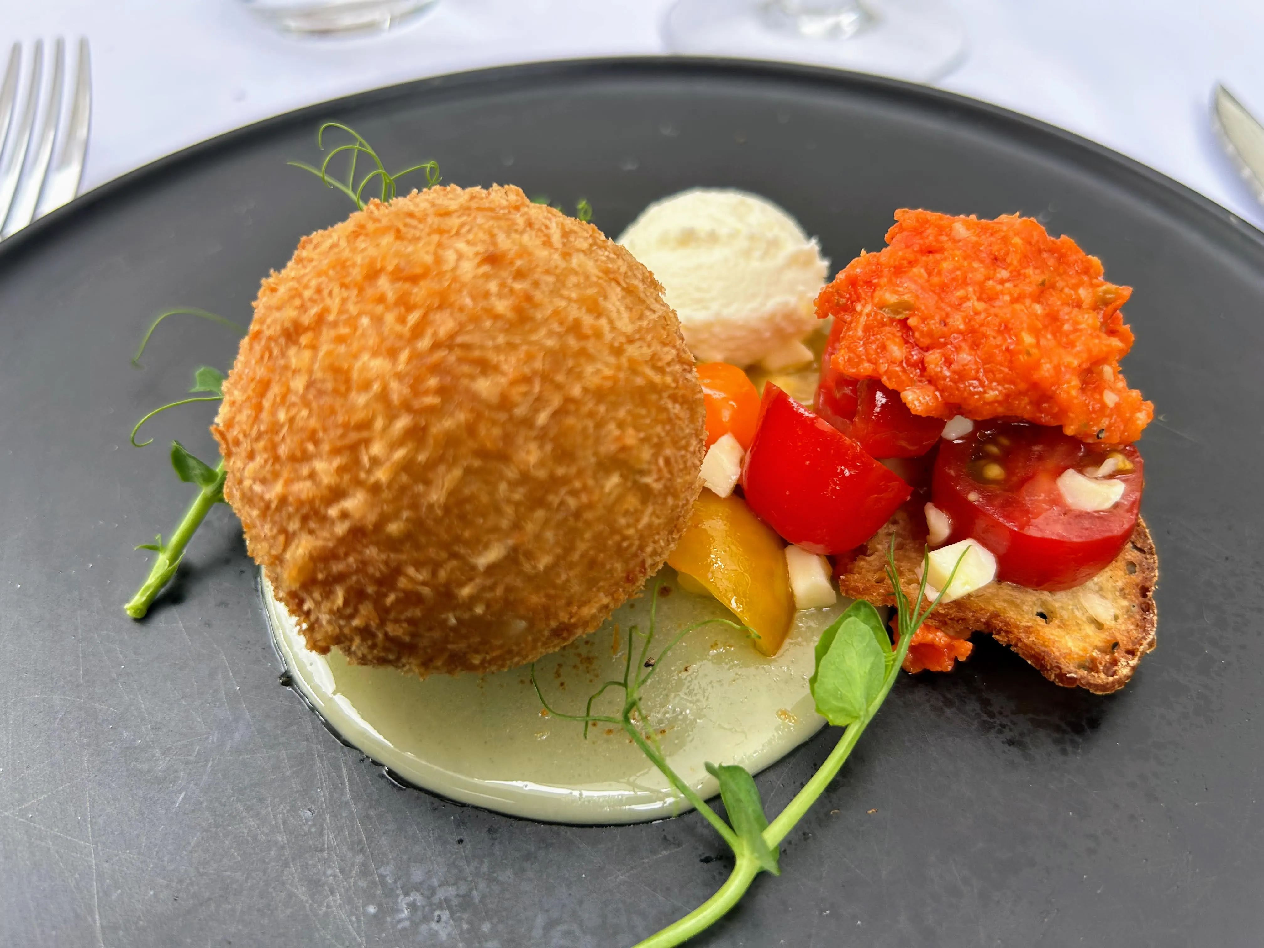 Croquette dorée, tomates cerises et crème, assiette noire