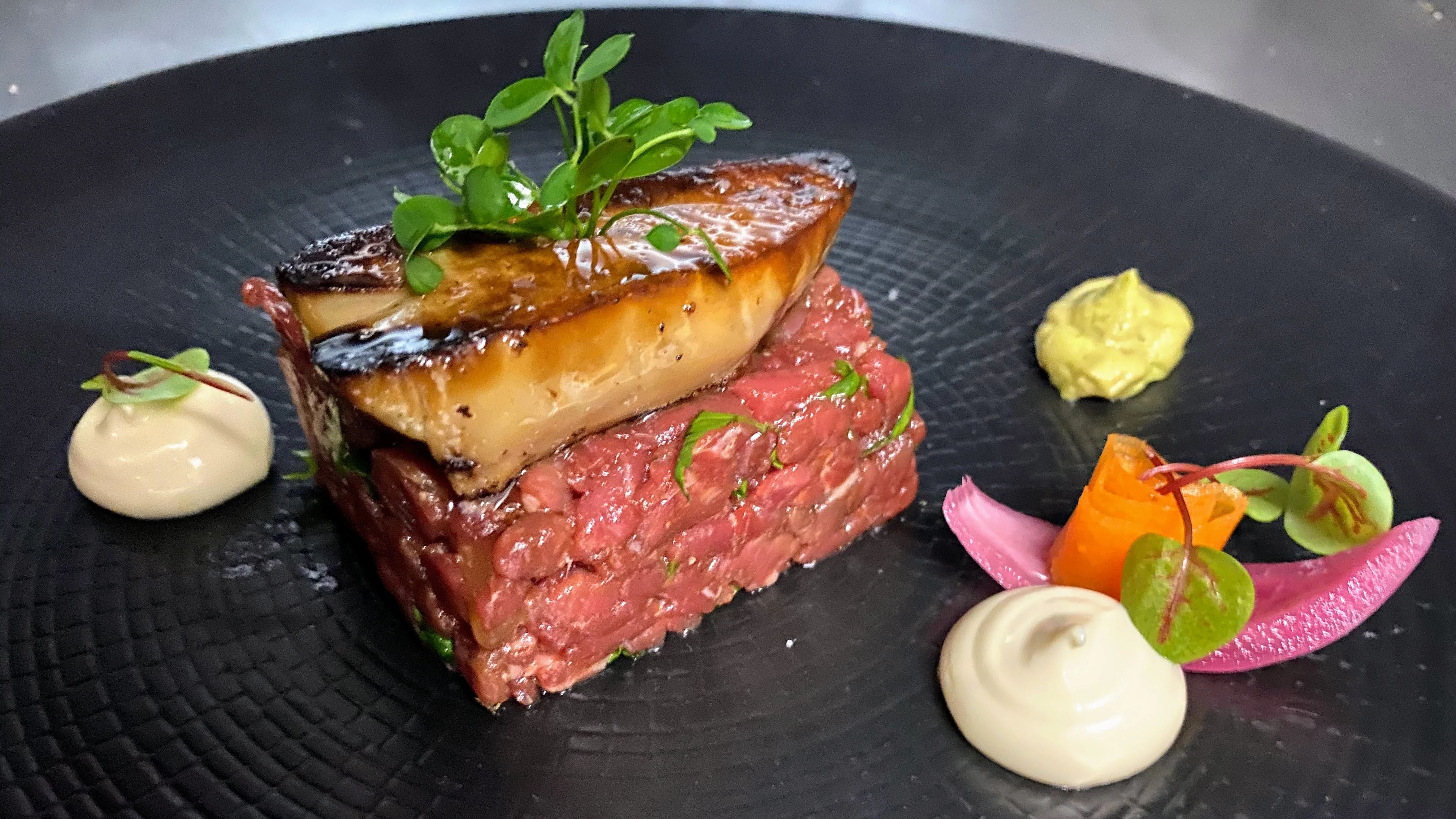 Foie gras poêlé posé sur un tartare de bœuf, assiette noire